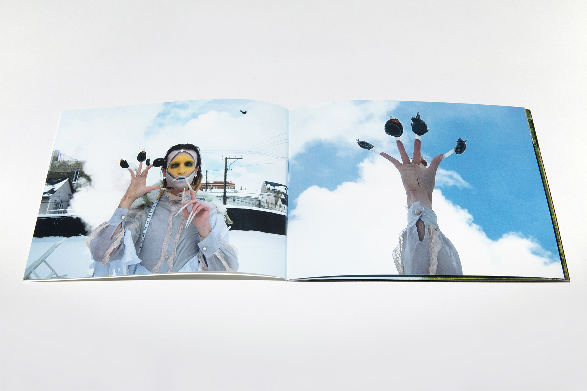 Two page spread in Imago depicting a figure in white and yellow facepaint with long nails on a snowy rooftop